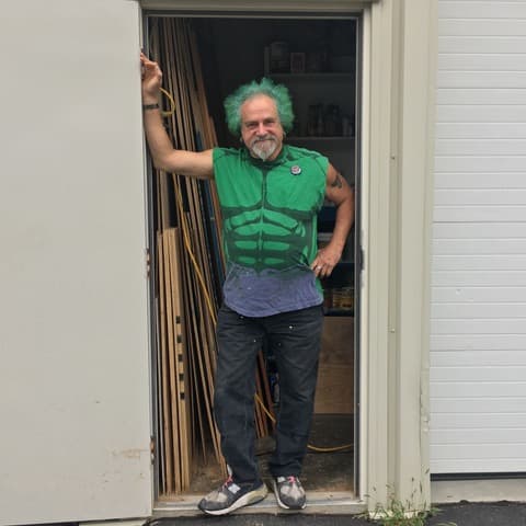 Joseph Weinberg — green hair and all — standing in the doorway of his Madison woodshop, milled trim stacked behind him